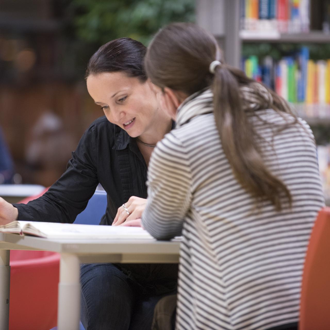 Zwei Frauen sitzen an einem Tisch und betrachten ein Buch